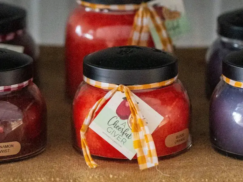 A row of colorful, round glass candles with black lids, adorned with checkered ribbons and labels. The cozy display evokes warmth and comfort.