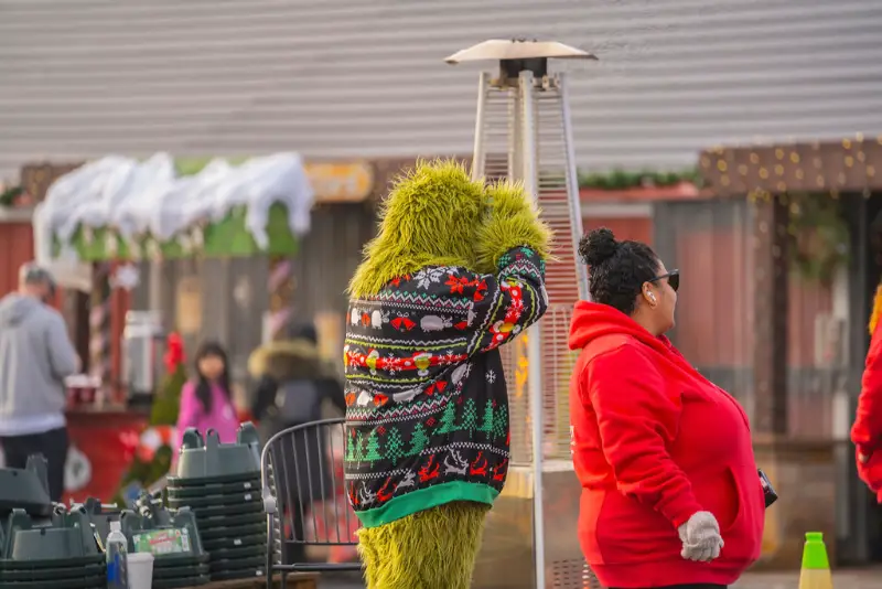 Festive characters in holiday sweaters near outdoor heater.